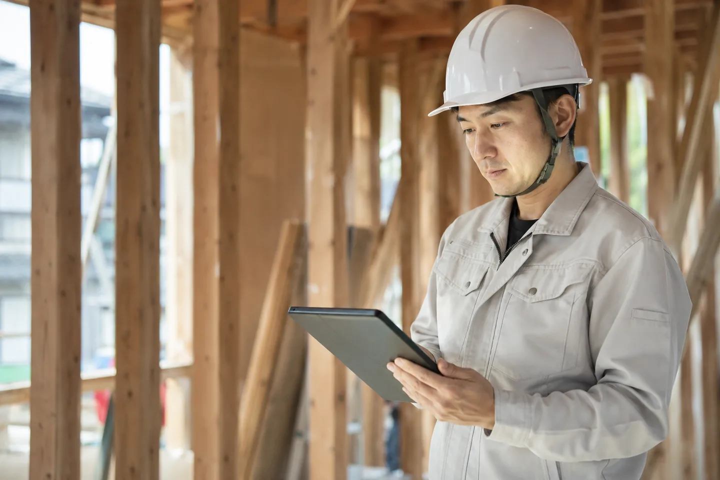 木造住宅の建築現場でタブレットを操作する作業着姿のスタッフ